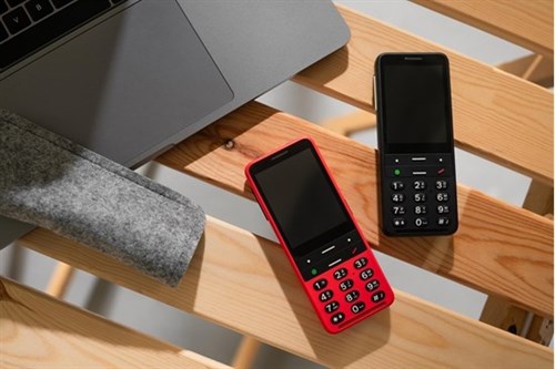 Na Zdjęciu Dwa Telefony Blind Shell Classic 2 Z Czerwoną I Czarną Obudową , Leżą Na Drewnianej Ławce Obok Laptopa.