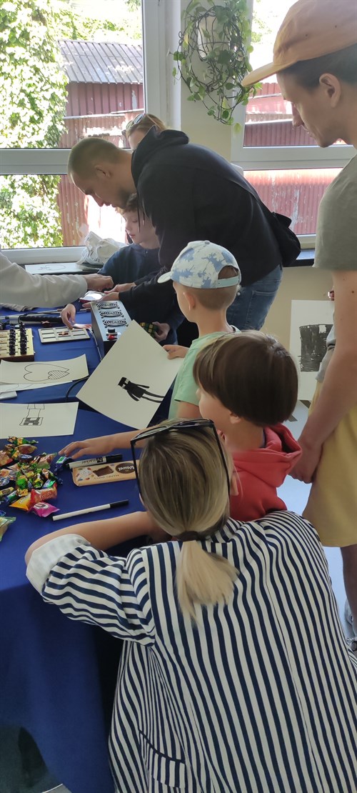 Grupka dzieci oraz ich rodziców czeka w kolejce ze swoimi rysunkami do wygrzewarki Zy-Fuse.