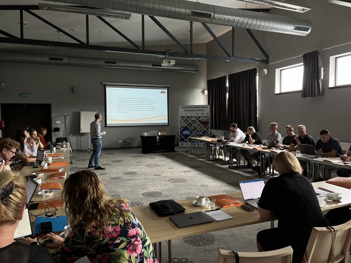 Prezes firmy Altix Adam Kalbarczyk prowadzi szkolenie. Uczestnicy szkolenia siedzą przy stołach ułożonych w literę w kształt litery U.