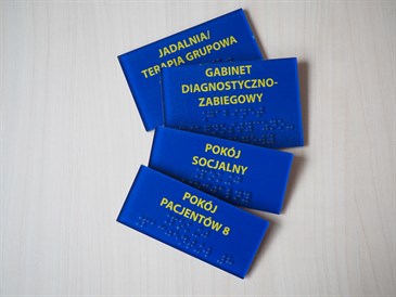 niebieskie tabliczki informacyjne z czarno drukiem i brajlem