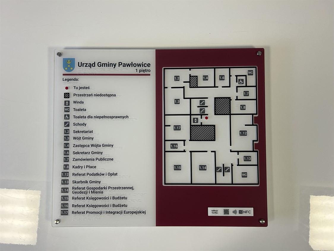 Dotykowy plan pierwszego piętra Urzędu Gminy Pawłowice z wypukłym układem pomieszczeń, opisami brajlowskimi, legendą funkcji oraz oznaczeniem 'Tu jesteś'. Zawiera także kody QR i NFC.